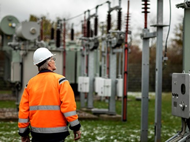 Man in orange safety jacket and a white safety helmet inspecting an electricity facility