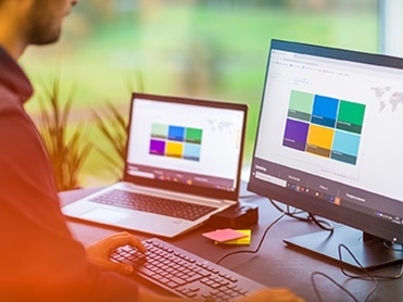 Man sitting at an office desk looking at analytic software on two screens.