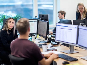 A man teaching two people about services at his desk, with all three looking at his monitor.